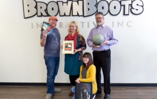 Four employees holding their works in front of a BrownBoots Interactive sign