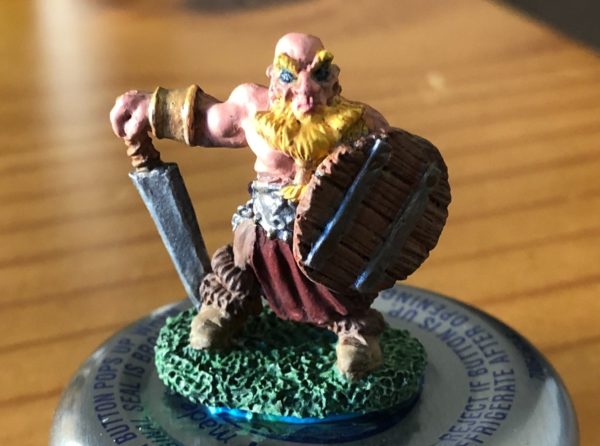 Painted miniature of a bald, muscular gnome wielding a sword and shield